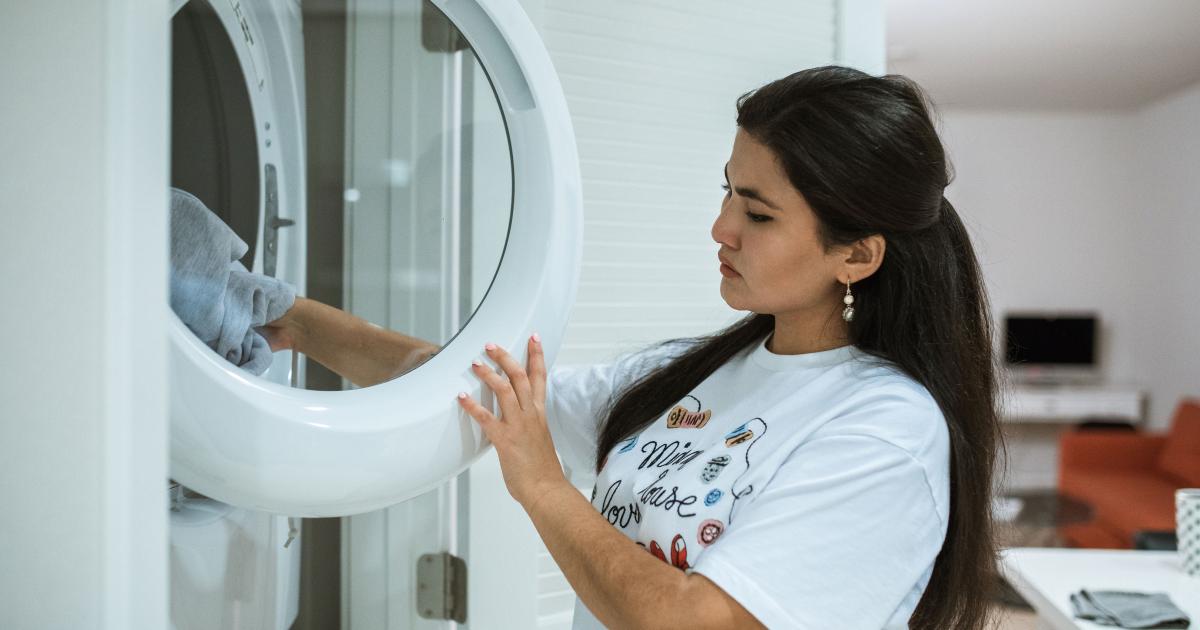 Ruka stahující silnou vrstvu šedého prachu z filtru sušičky