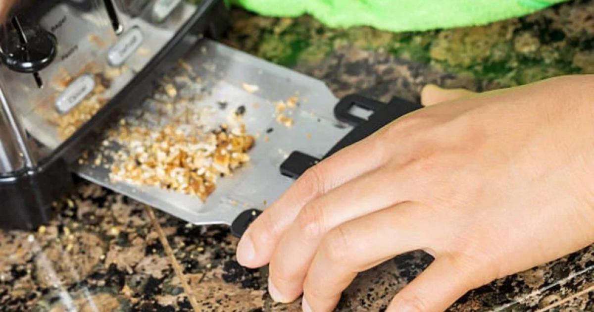 Ruce vysouvající kovovou misku na drobky ze spodní části černého topinkovače