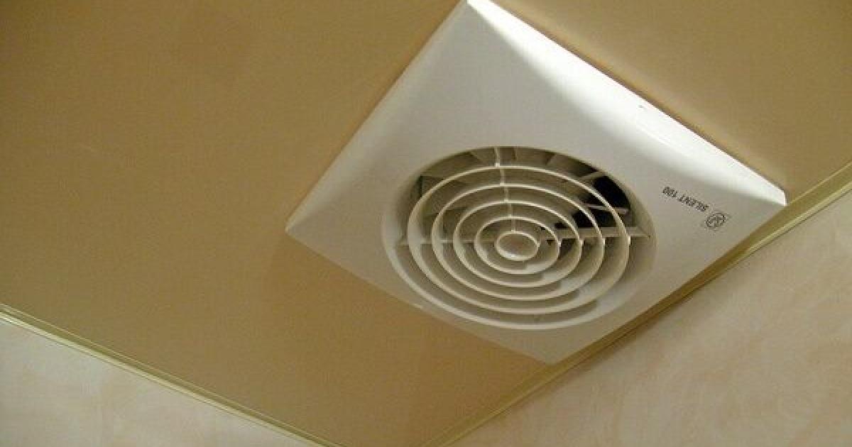 Zaprášený kryt koupelnového ventilátoru na bílém stropě