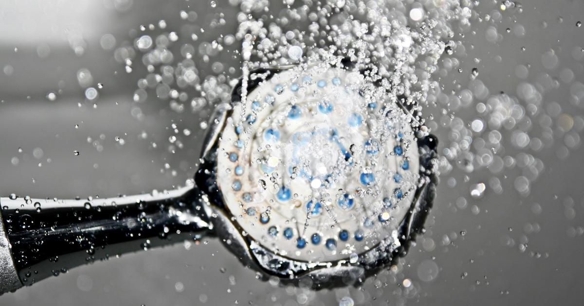 Odmontovaná sprchová hlavice ponořená v průhledné misce s octovým roztokem