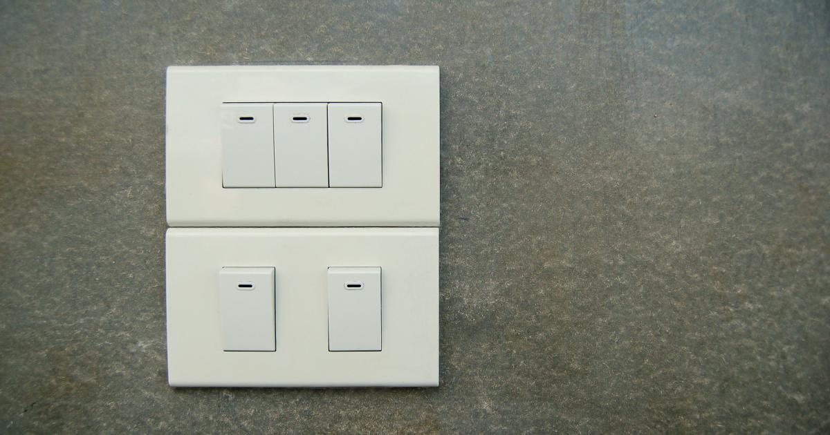 Ruka v modrém hadříku z mikrovlákna jemně otírá čistý bílý dvojvypínač