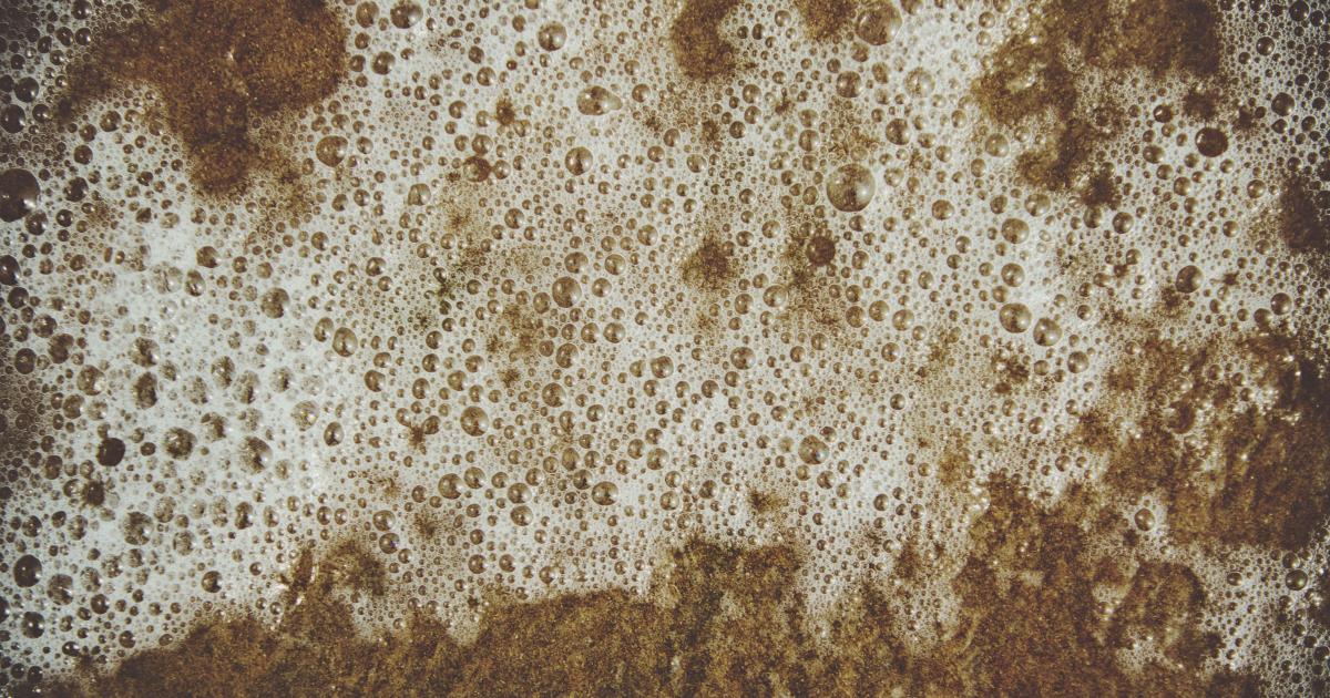 Ruka utírající mastnotu na horní části kuchyňské skříňky pomocí hadříku z mikrovlákna